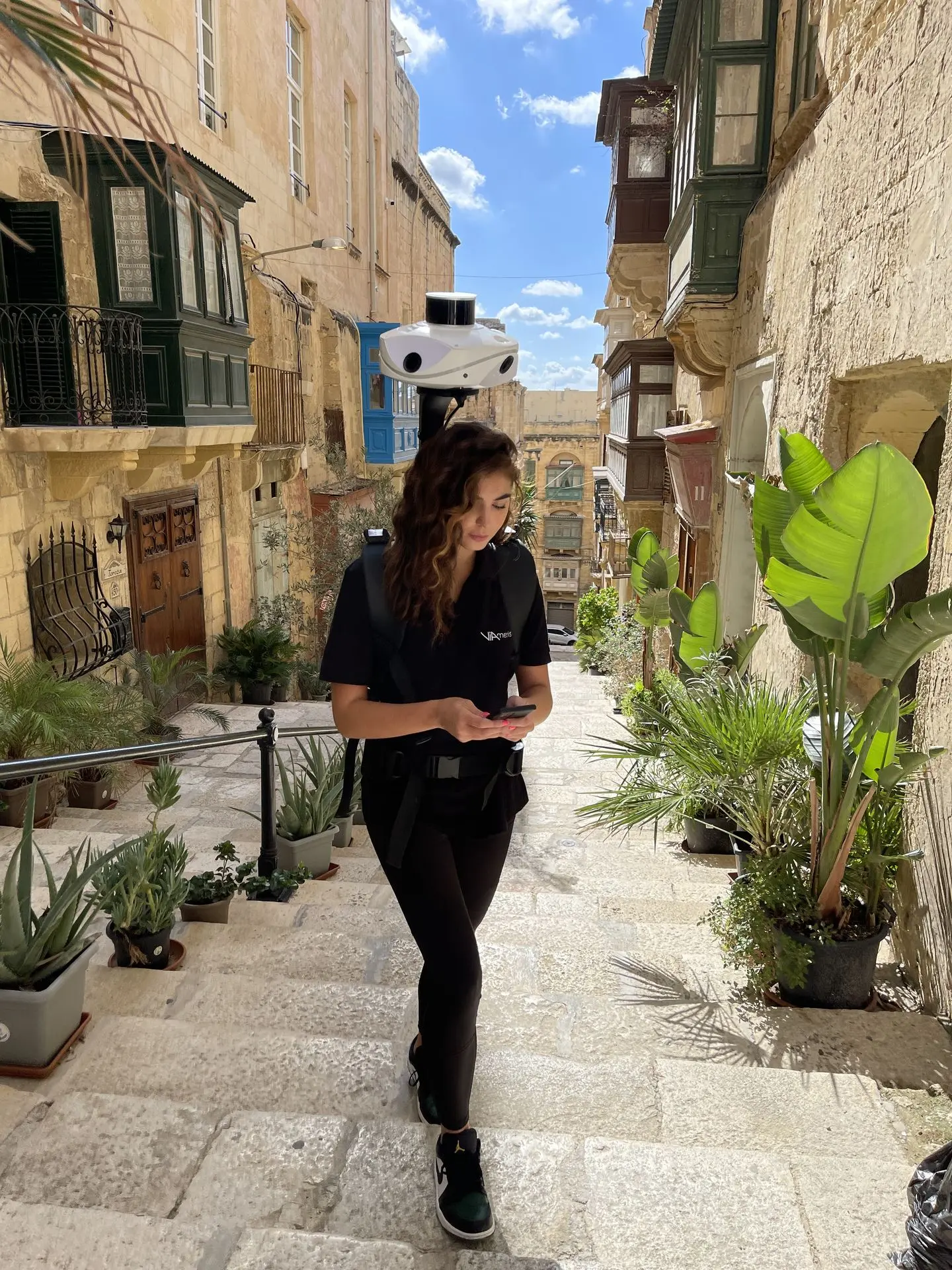 Une femme porte le scanner LiDAR Viametris MS-96 en sac à dos tout en scannant une ruelle en escalier et en contrôlant les données directement sur son smartphone.