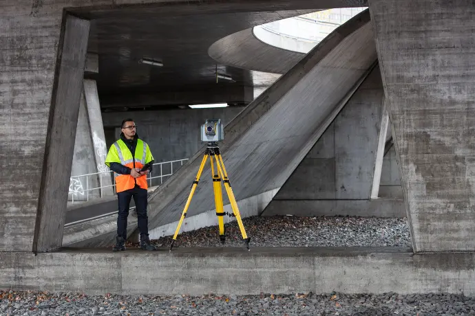 Een landmeter voert een infrastructuurmeting uit met de Trimble SX12 onder een brug, waarbij total station precisie wordt gecombineerd met scanning voor revisiebeheer.